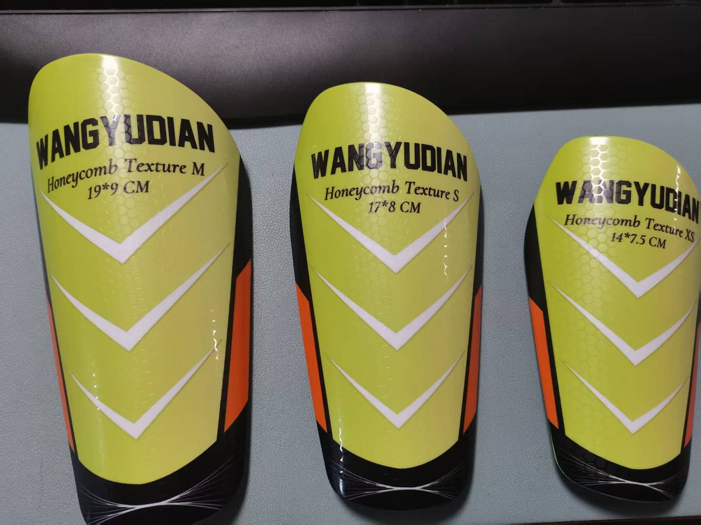 Honeycomb full-size shin guards labelled M 19 × 9 cm, S 17 × 8 cm and XS 14 × 7.5 cm