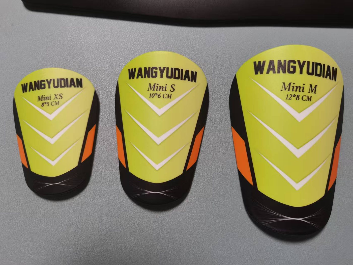 Mini shin guards labelled Mini XS 8 × 5 cm, Mini S 10 × 6 cm and Mini M 12 × 8 cm