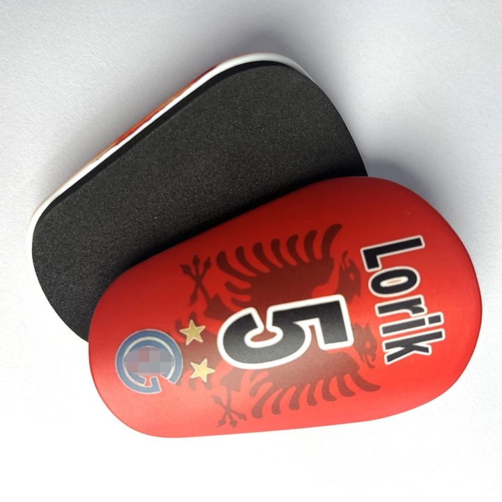Red mini shin guard printed 'Lorik 5' resting on its foam-lined back
