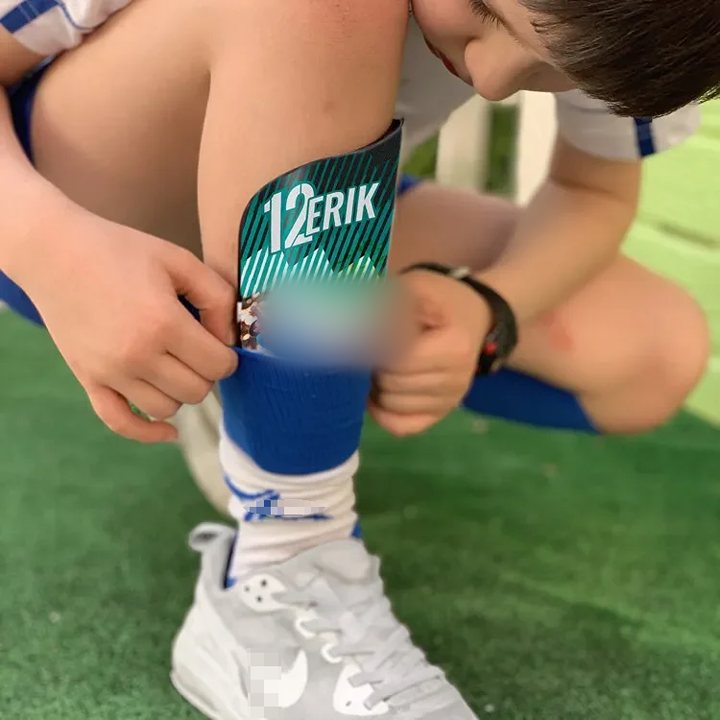 A printed shin guard '12 ERIK' being slipped into a football sock