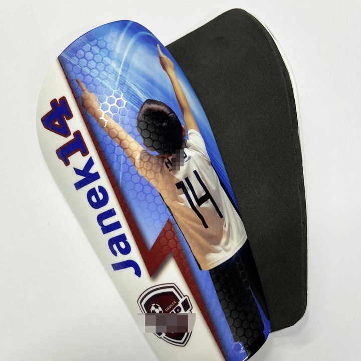Honeycomb-textured shin guard printed 'Janek 14' with a player photo, beside its foam-lined back