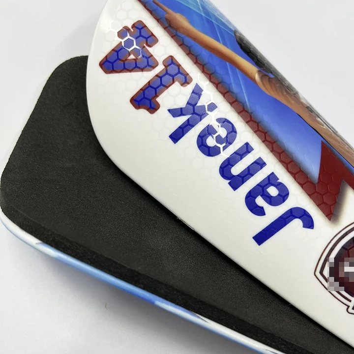 Close-up of the printed name and number on a honeycomb-textured shin guard, foam back behind