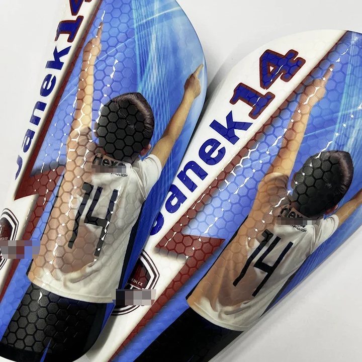 Pair of honeycomb-textured shin guards printed 'Janek 14' with a player photo, angled view