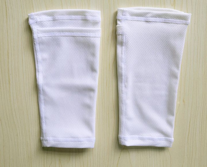 Pair of plain white knitted shin guard sleeves with pocket openings, on a wooden surface